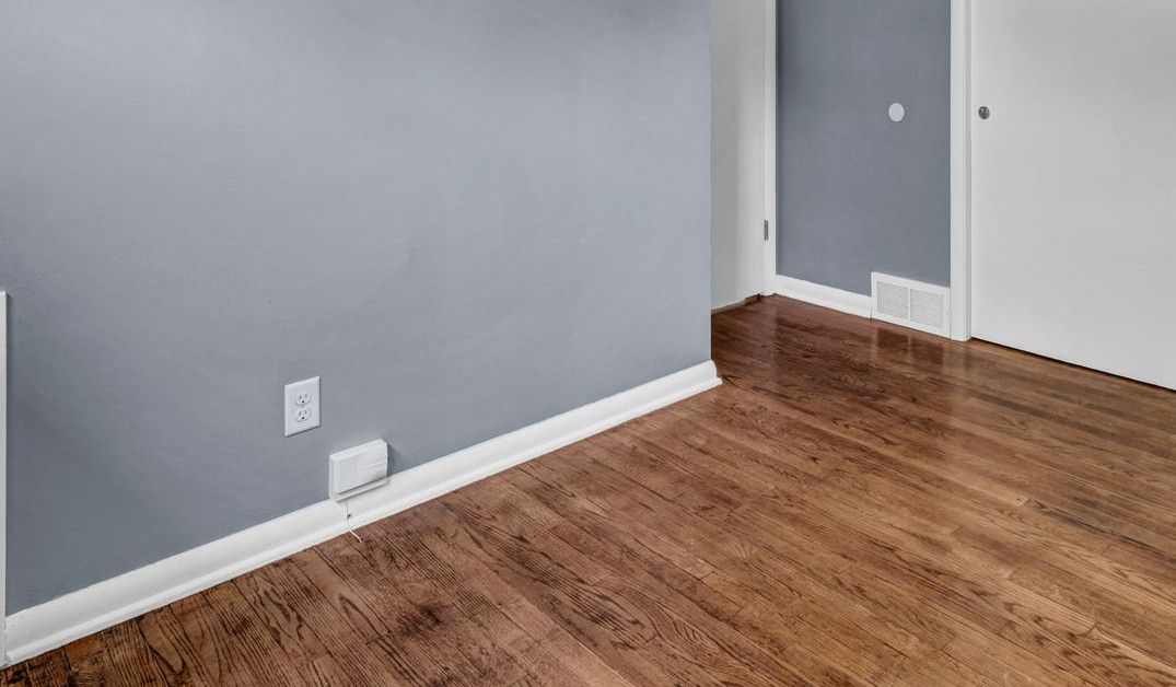 An empty room with blue walls, white sliding closet doors, and dark hardwood flooring